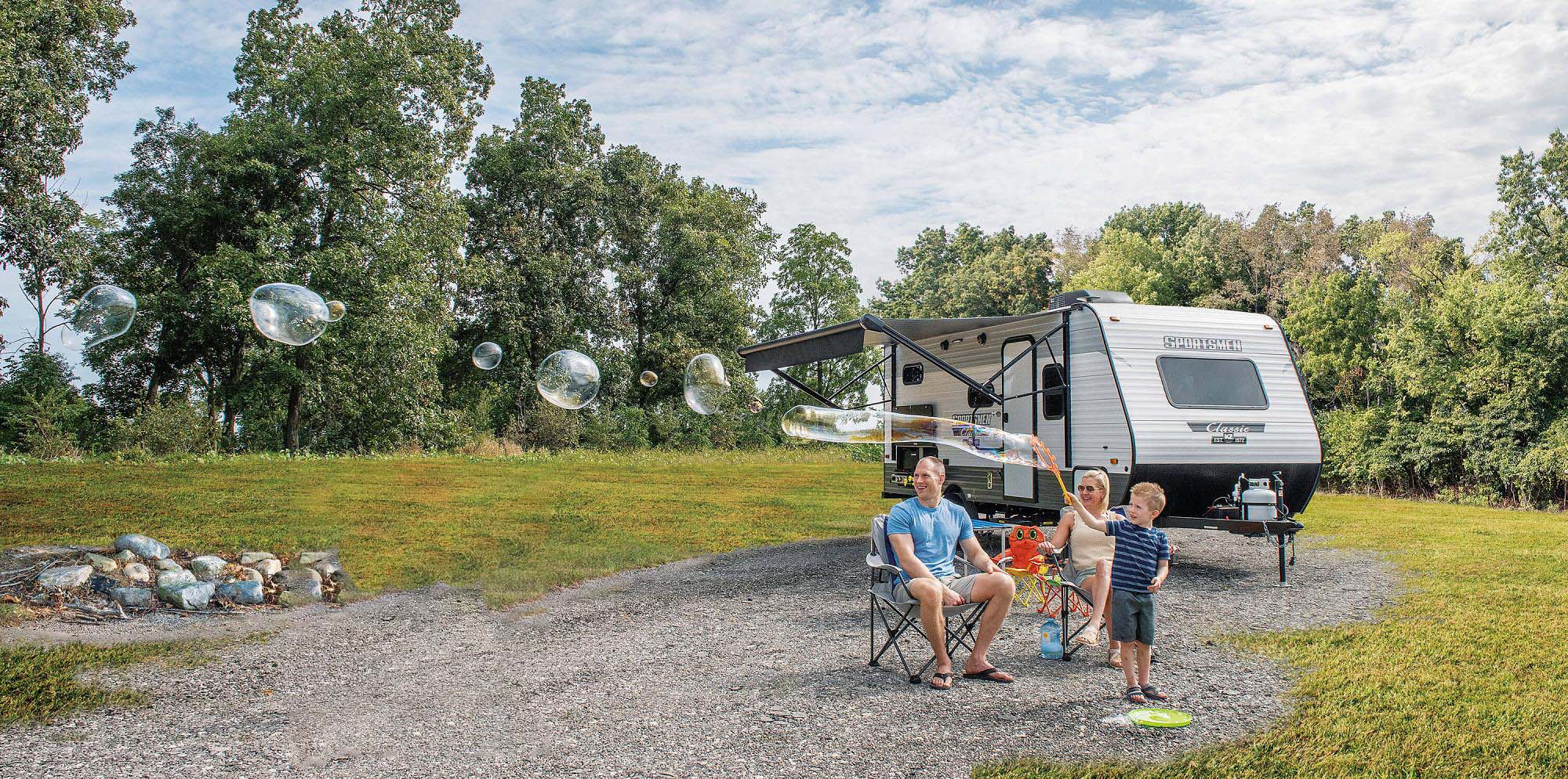 Family enjoying outdoor camping beside a travel trailer at a scenic campground.